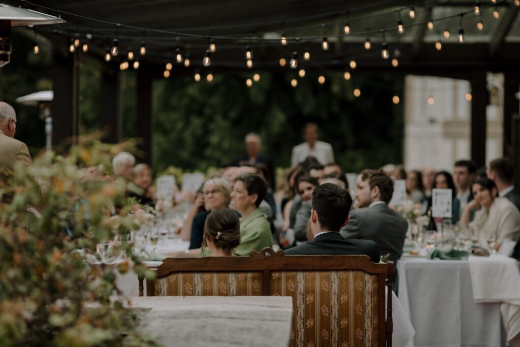 An outdoor wedding with string lights over the tablesof happy guests eating. 